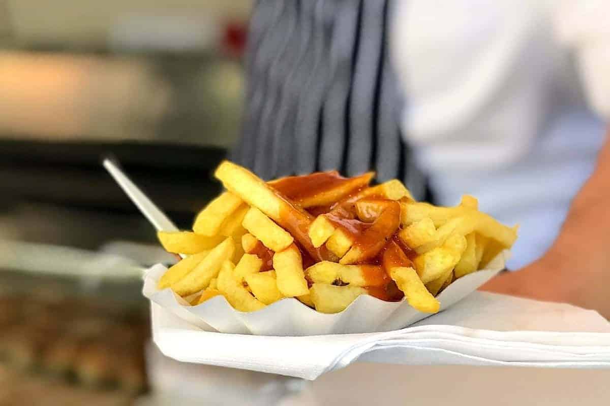 a paper plate with french fries topped with currywurst sauce.