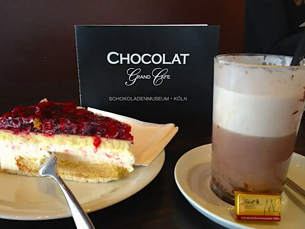 glass of hot chocolate and a slice of cheesecake on a plate.