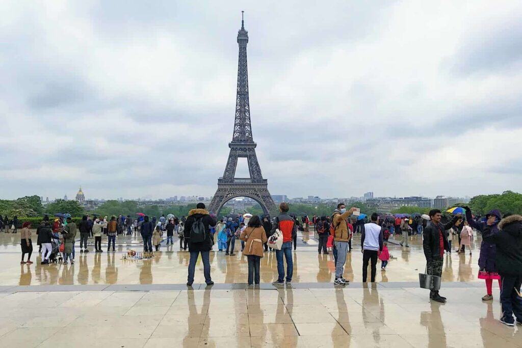 Eifffel tower with tourists milling about in the rain.