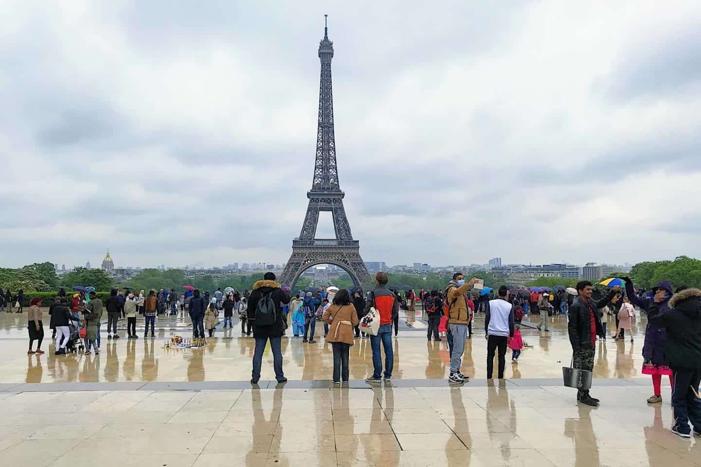Eifffel tower with tourists milling about in the rain.