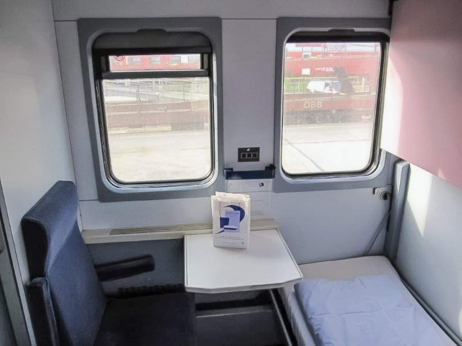 Sleeping compartment on Dacia Express with one chair and a small bunk bed with a duvet.